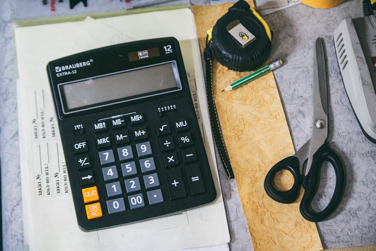 Hands typing an ingredient list into a laptop next to fresh produce and a calculator, using a nutrition calculator to work out recipe nutrition